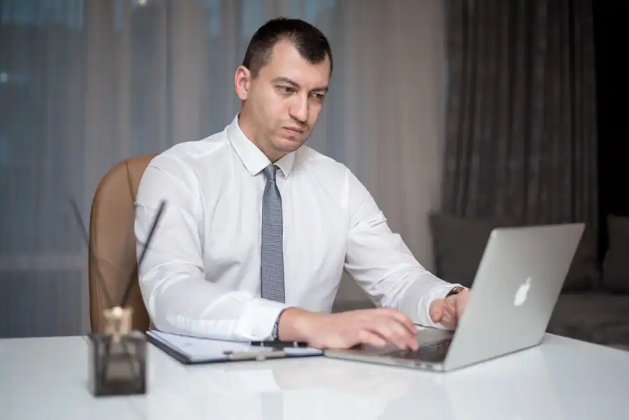 Professional businessman wearing a white shirt working on a laptop at an office desk indoors.